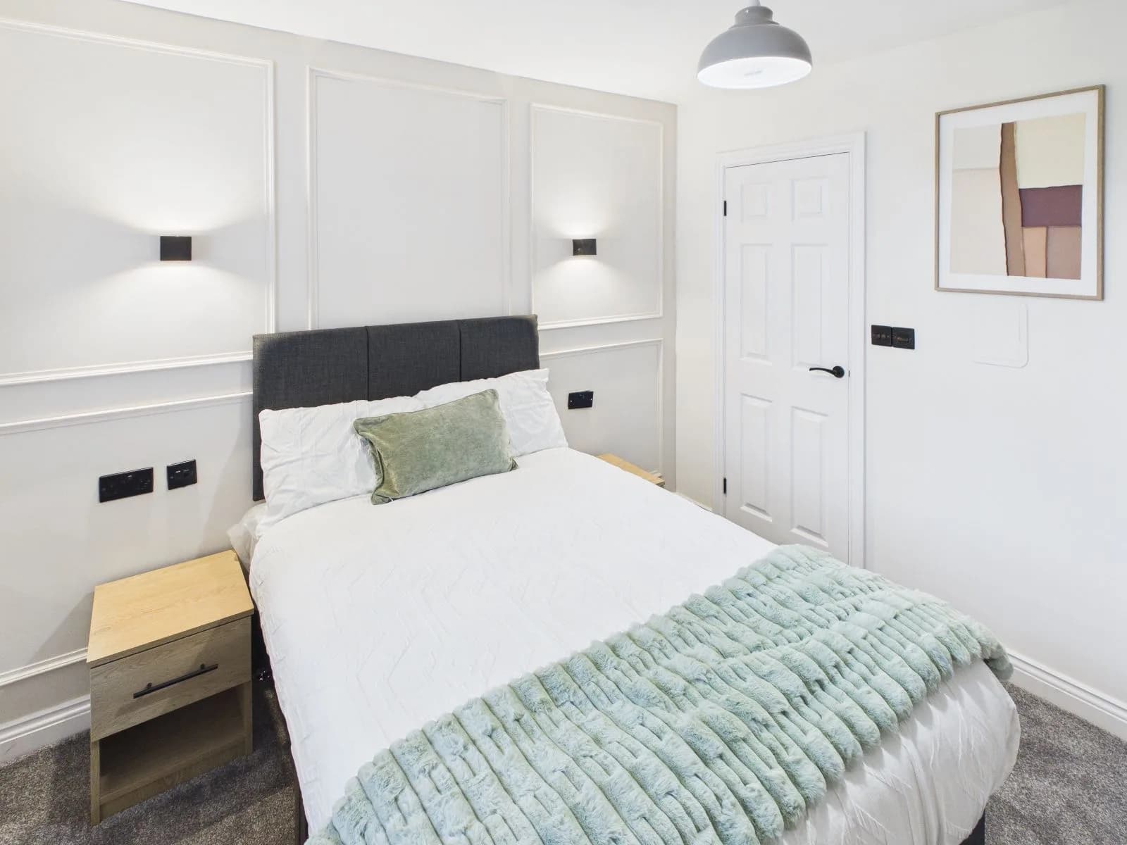 Bedroom with a panelled feature wall, wall lights and framed artwork at the completed Darlington HMO.